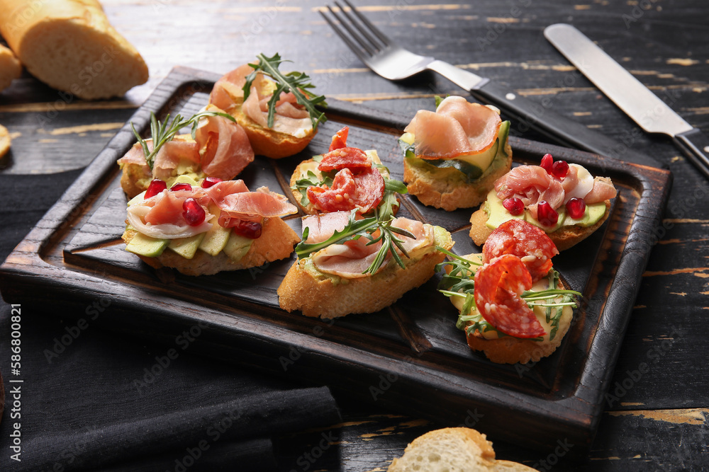 Board of tasty bruschettas with ham on dark wooden background