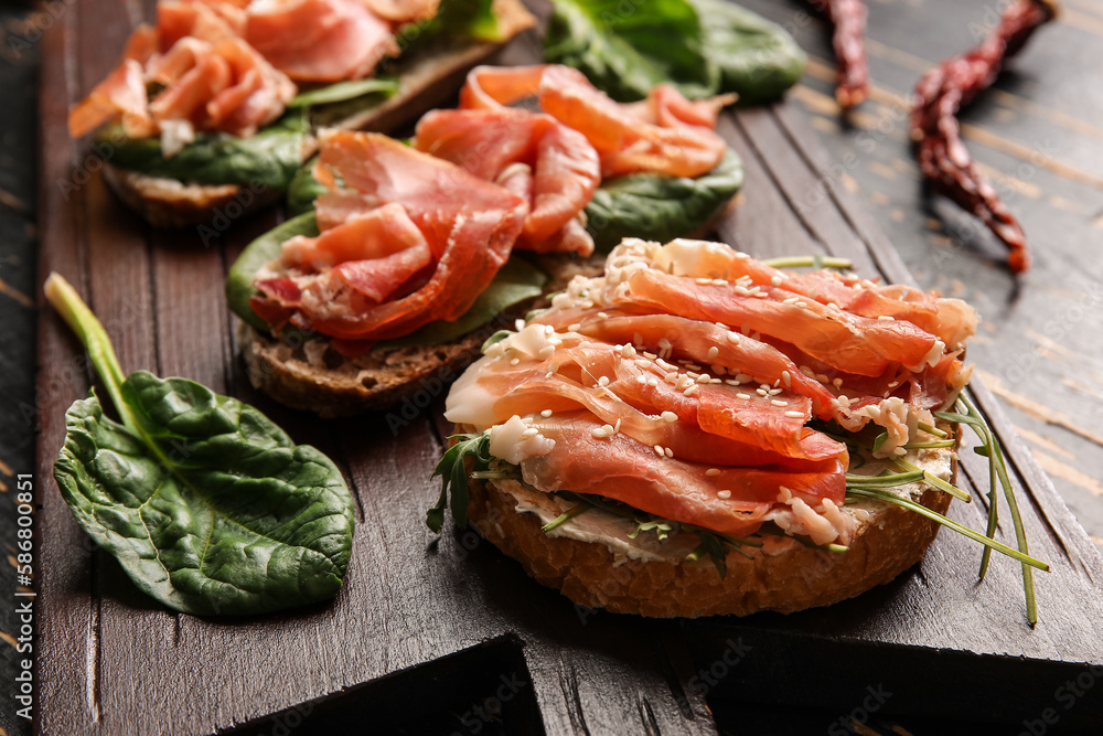 Boards of tasty bruschettas with ham on dark wooden background, closeup