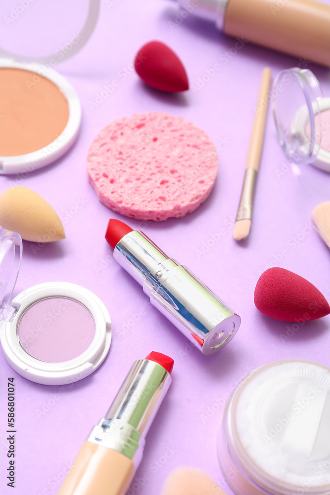 Lipsticks with makeup brush and sponges on lilac background, closeup