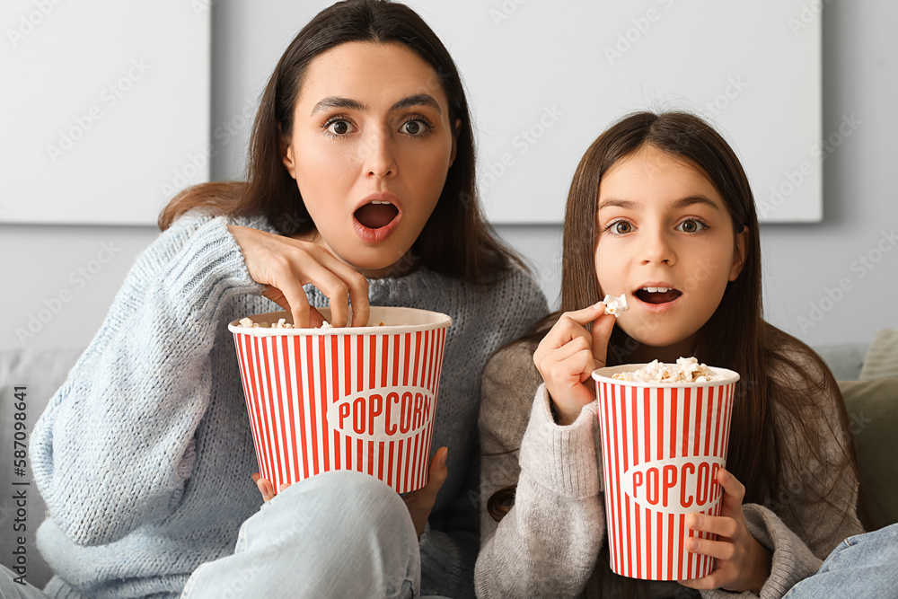 Little girl and her mother in warm sweaters with popcorn watching TV at home