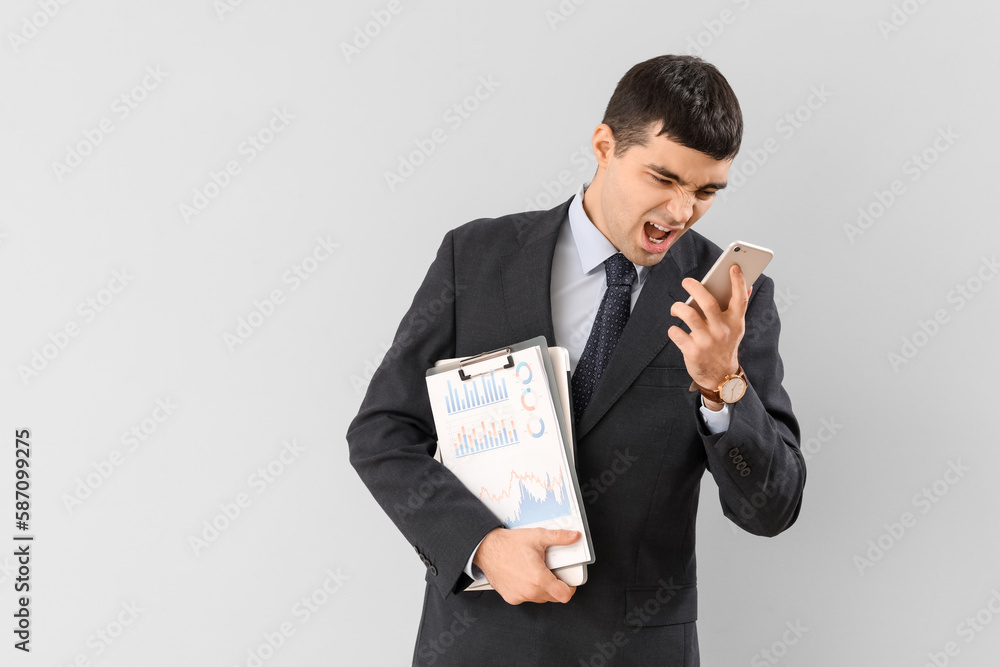 Angry screaming businessman with phone on light background