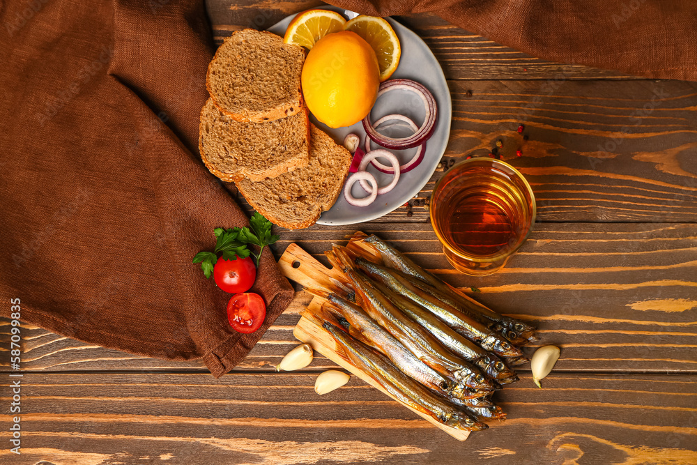 Board with delicious smoked capelin, glass of beer and plate with snacks on wooden background