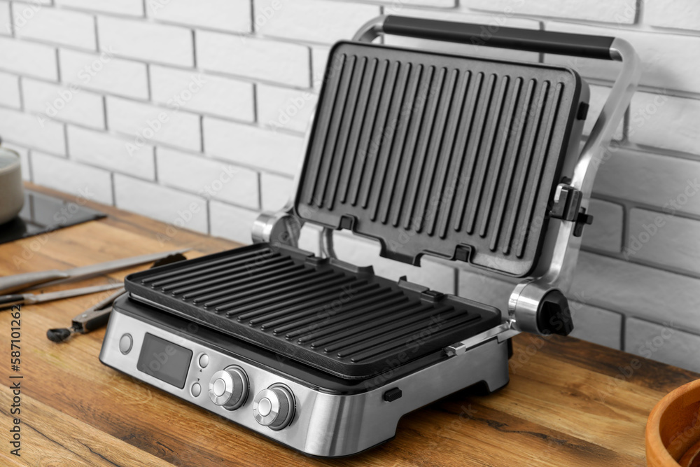 Modern electric grill on table near white brick wall