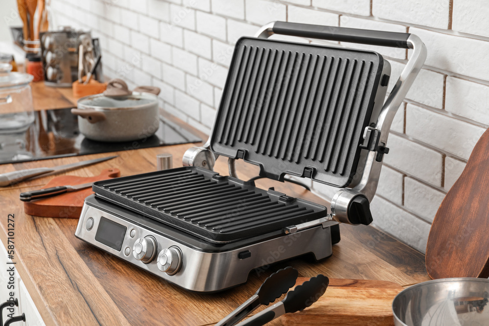 Modern electric grill on table near white brick wall