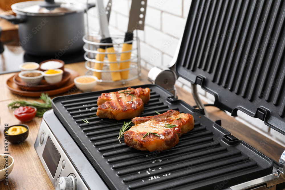 Modern electric grill with tasty steaks on table near white brick wall