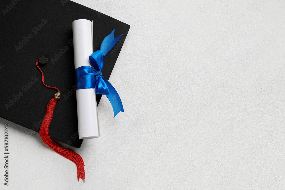 Diploma with blue ribbon and graduation hat on white table