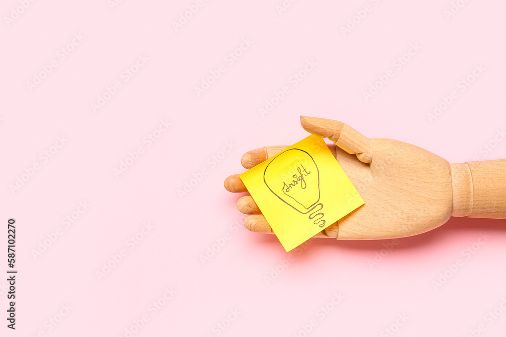 Wooden hand and sticky paper with drawn light bulb on pink background