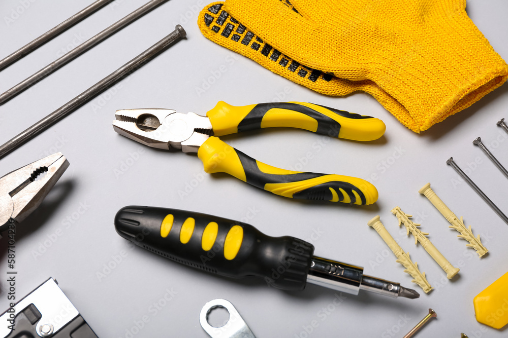 Pliers, screwdriver and gloves on grey background