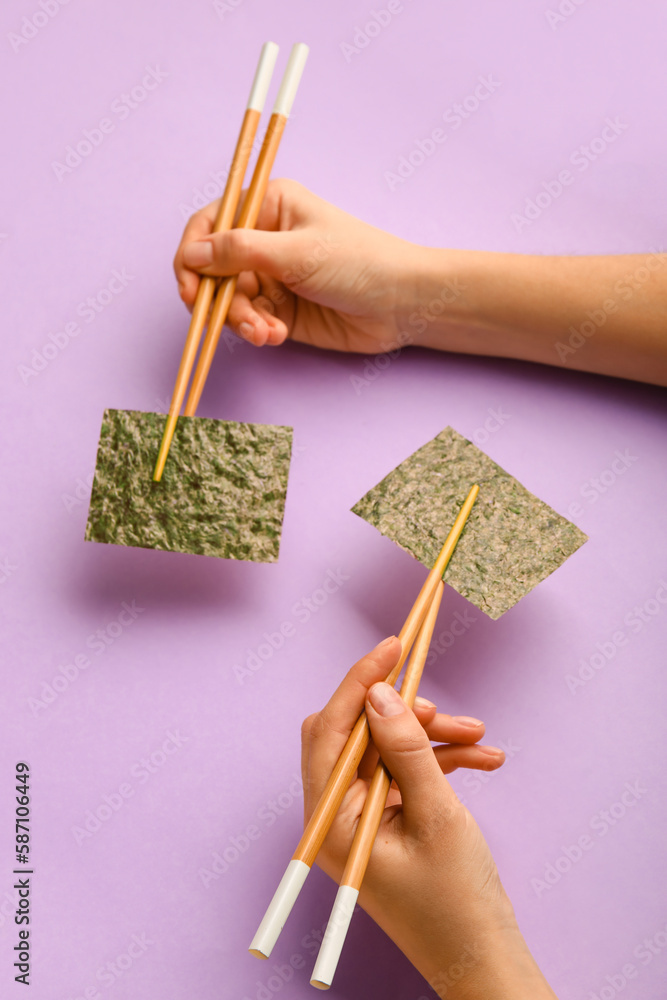 Woman holding chopsticks with nori sheets on color background