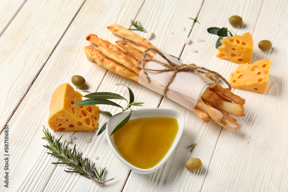 Bunch of tasty Italian Grissini, cheese and bowl with oil on light wooden background