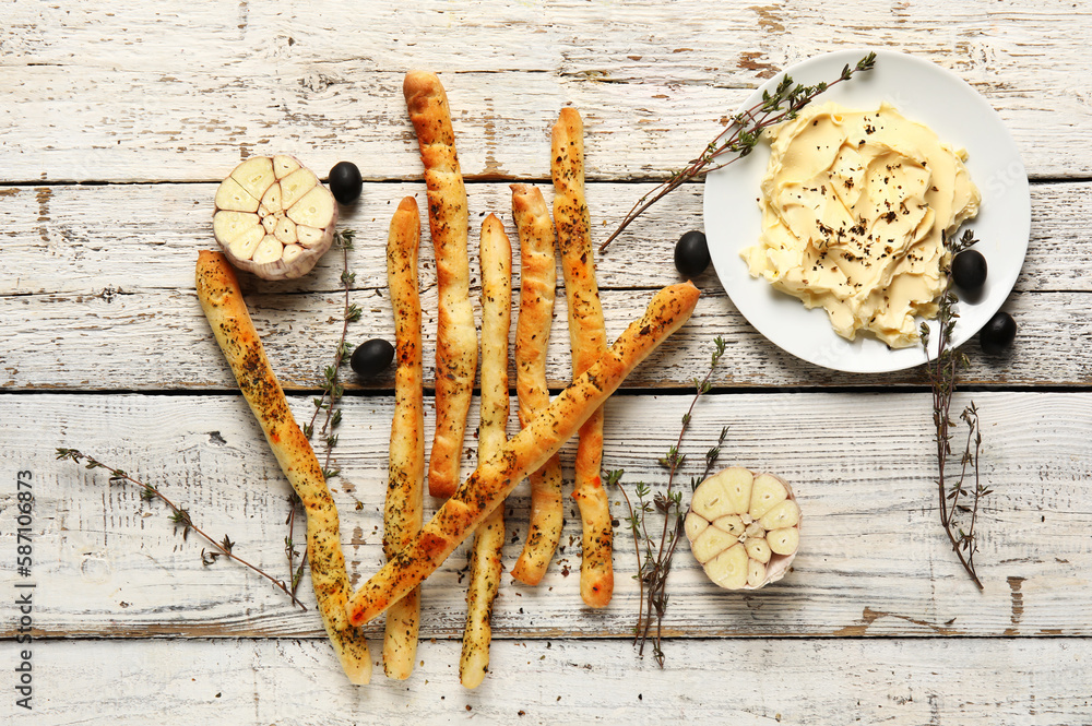 Tasty Italian Grissini and plate with butter on light wooden background