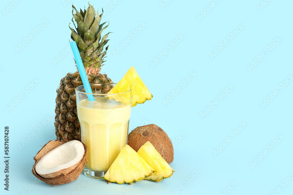 Glass of tasty pineapple smoothie, straw and coconut on blue background