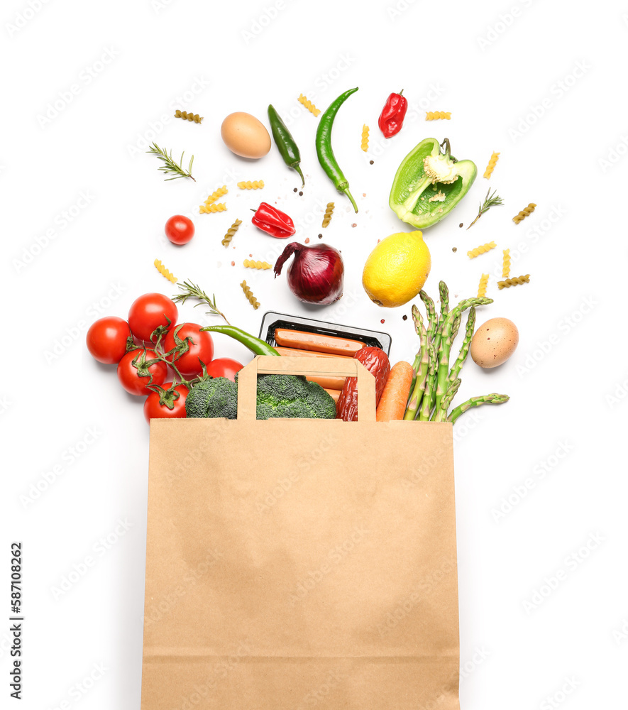 Paper bag with vegetables and sausages on white background