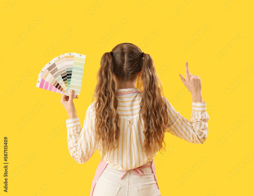 Female artist with paint color palettes pointing at something on yellow background, back view