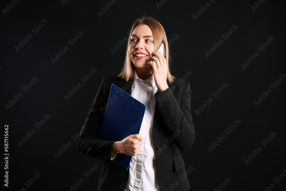 Female business consultant with clipboard talking by mobile phone on black background