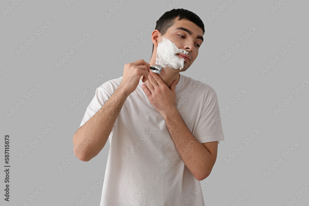 Young man shaving against light background