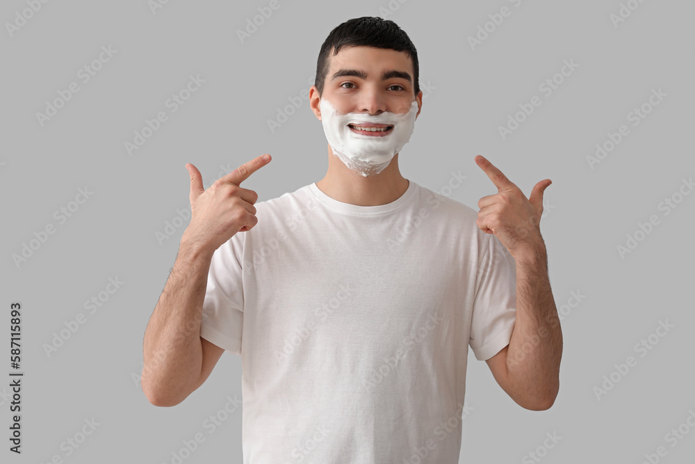 Young man with shaving foam on face against light background