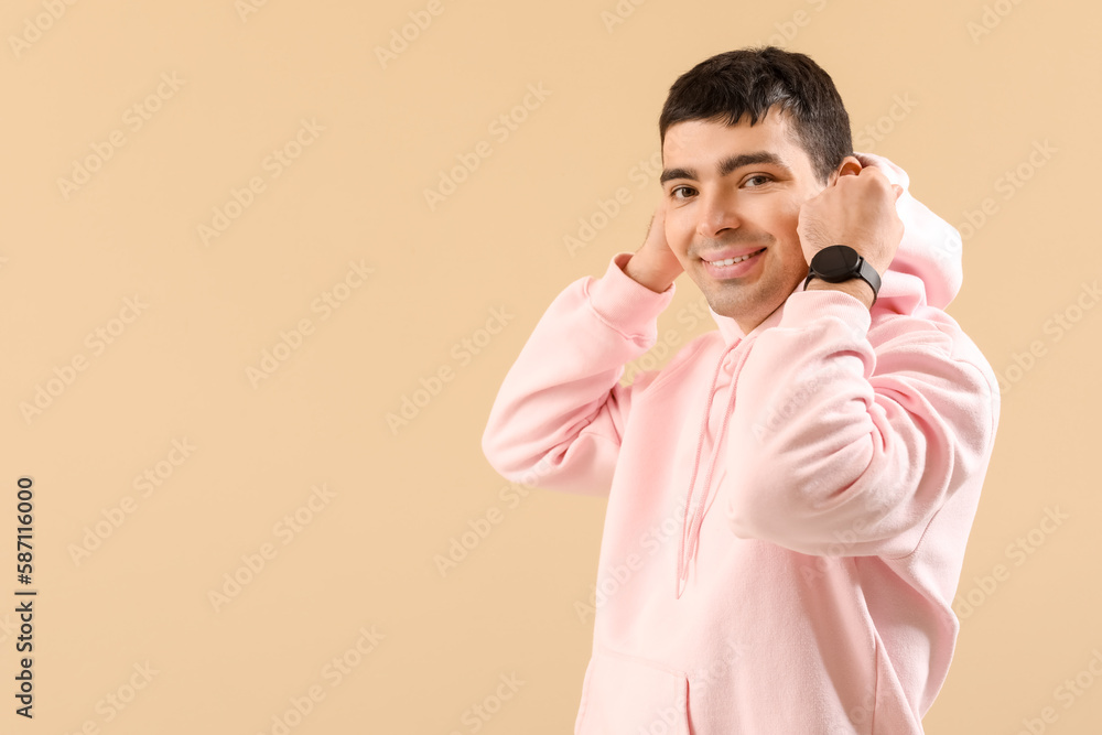 Stylish young man in hoodie and with watch on beige background