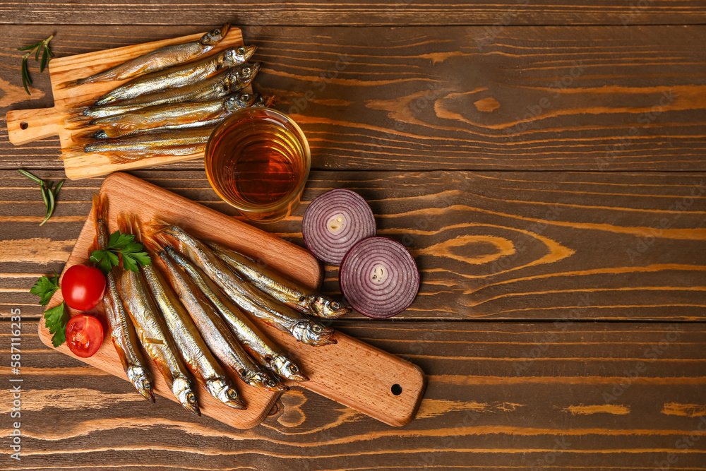 Boards with delicious smoked capelin and glass of beer on wooden background