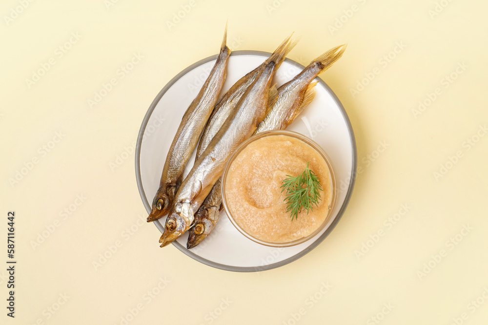 Plate with bowl of caviar and smoked capelin fishes on beige background