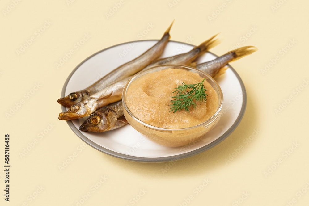 Plate with bowl of caviar and smoked capelin fishes on beige background