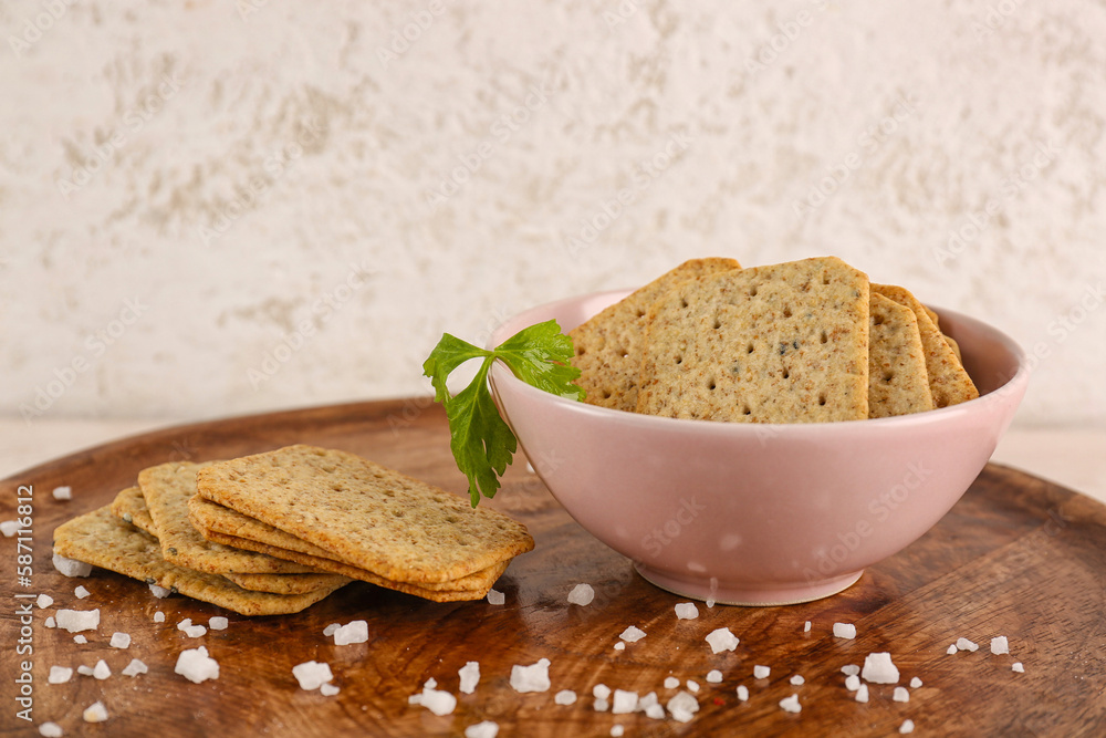 Bowl tasty crackers, salt and parsley on board against grey wall