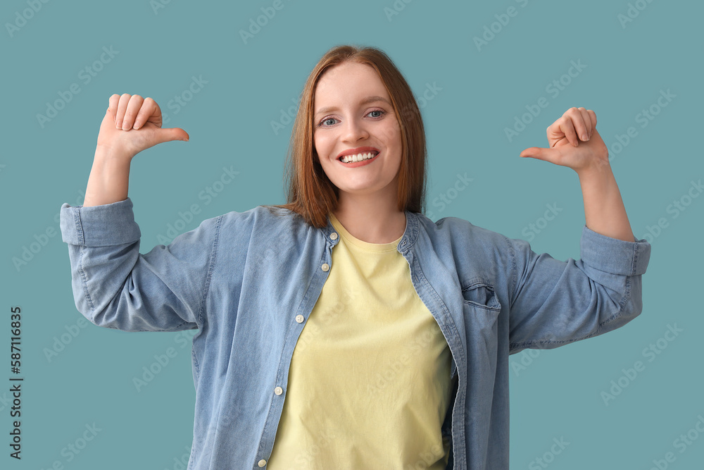 Beautiful redhead woman pointing at herself on blue background