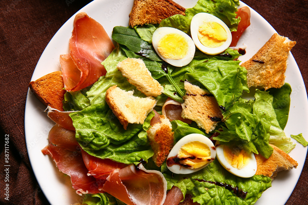 Plate of delicious salad with boiled eggs, jamon and croutons on brown napkin, closeup