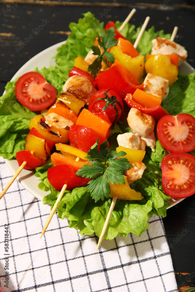 Plate with grilled chicken skewers and vegetables on dark wooden background