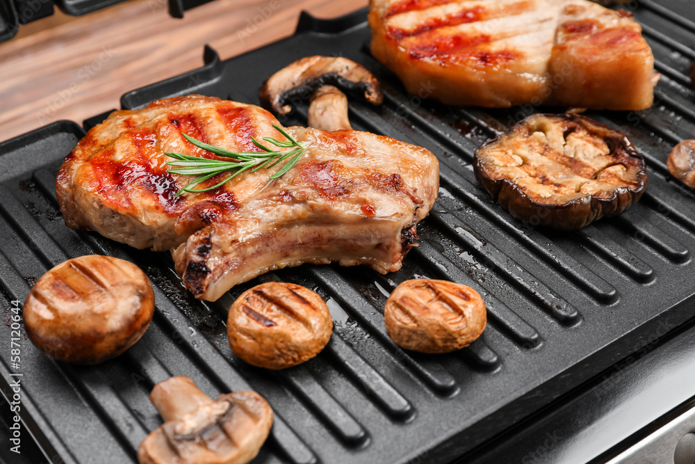 Modern electric grill with tasty steaks and vegetables on table, closeup