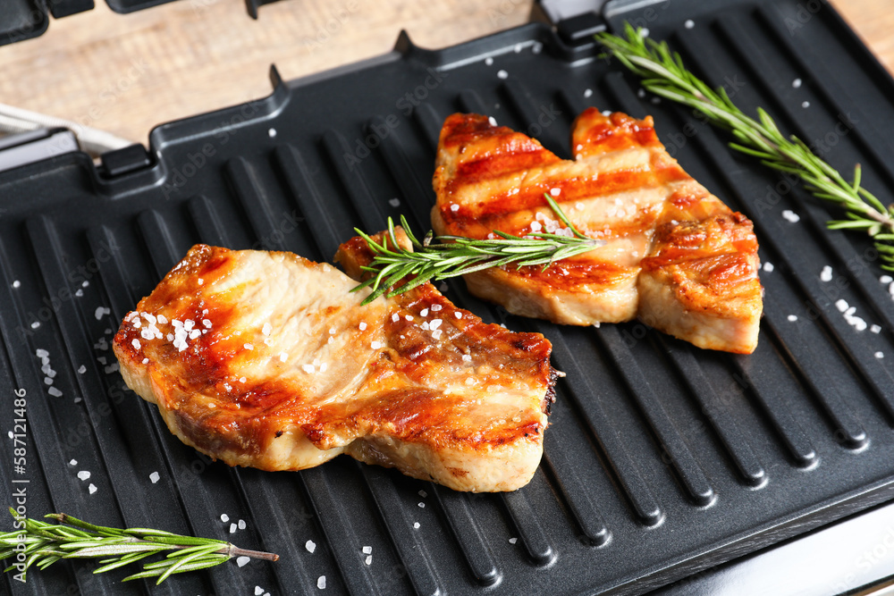 Modern electric grill with tasty steaks on wooden background, closeup