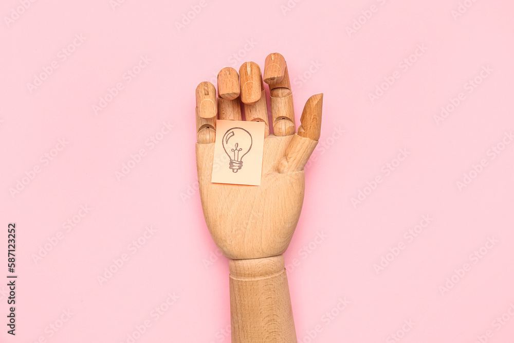 Wooden hand and sticky paper with drawn light bulb on pink background. Insight concept