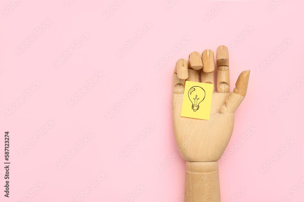 Wooden hand and sticky paper with drawn light bulb on pink background. Insight concept