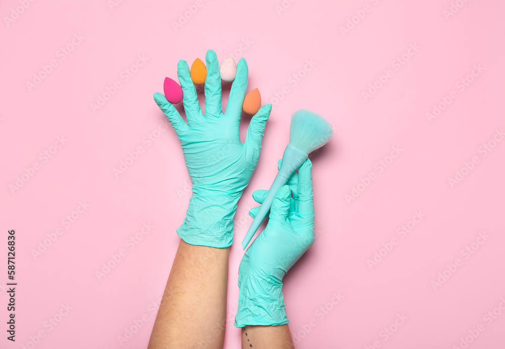 Makeup artist in rubber gloves with sponges and brush on pink background