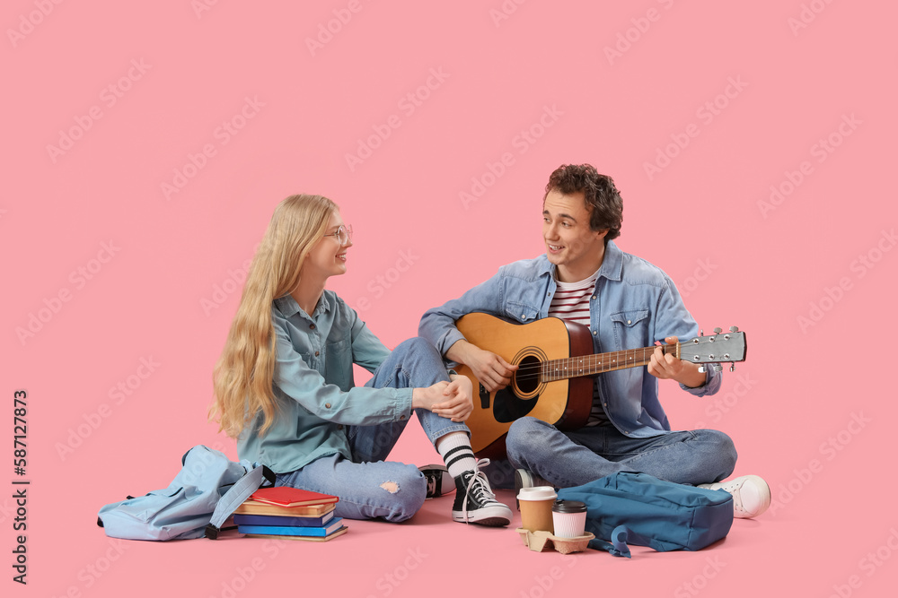 Teenage girl with her boyfriend playing guitar on pink background