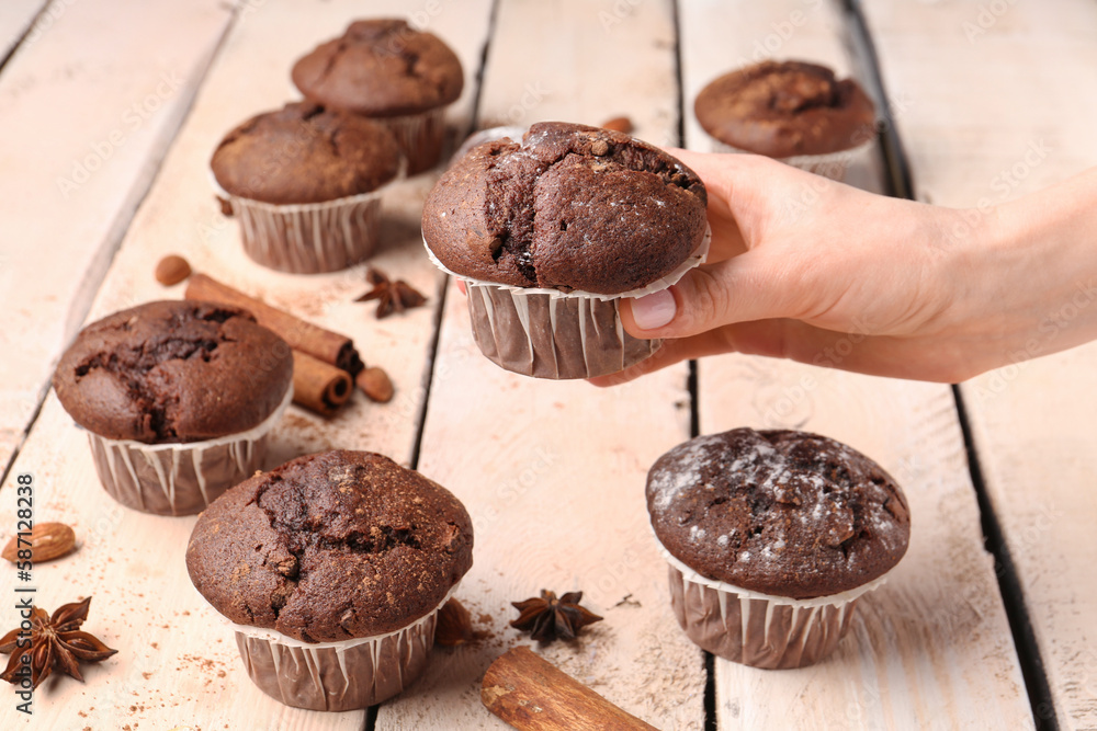 Woman holding tasty chocolate cupcake on light wooden background