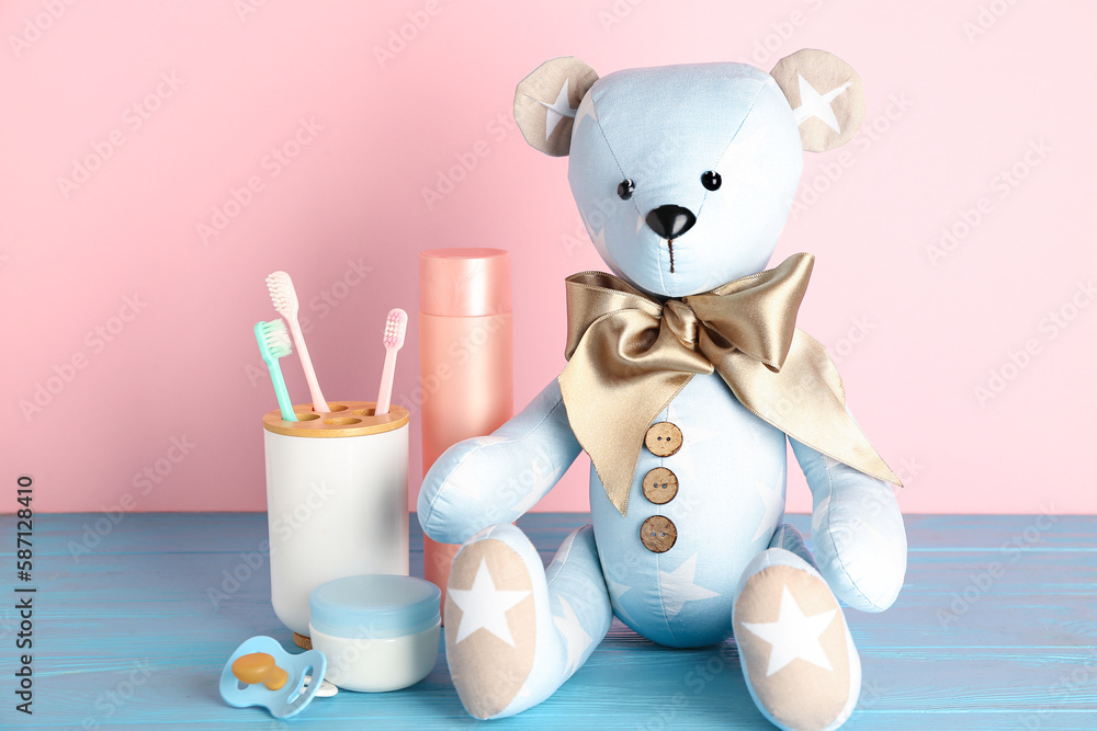 Toy bear with baby accessories on table near pink wall