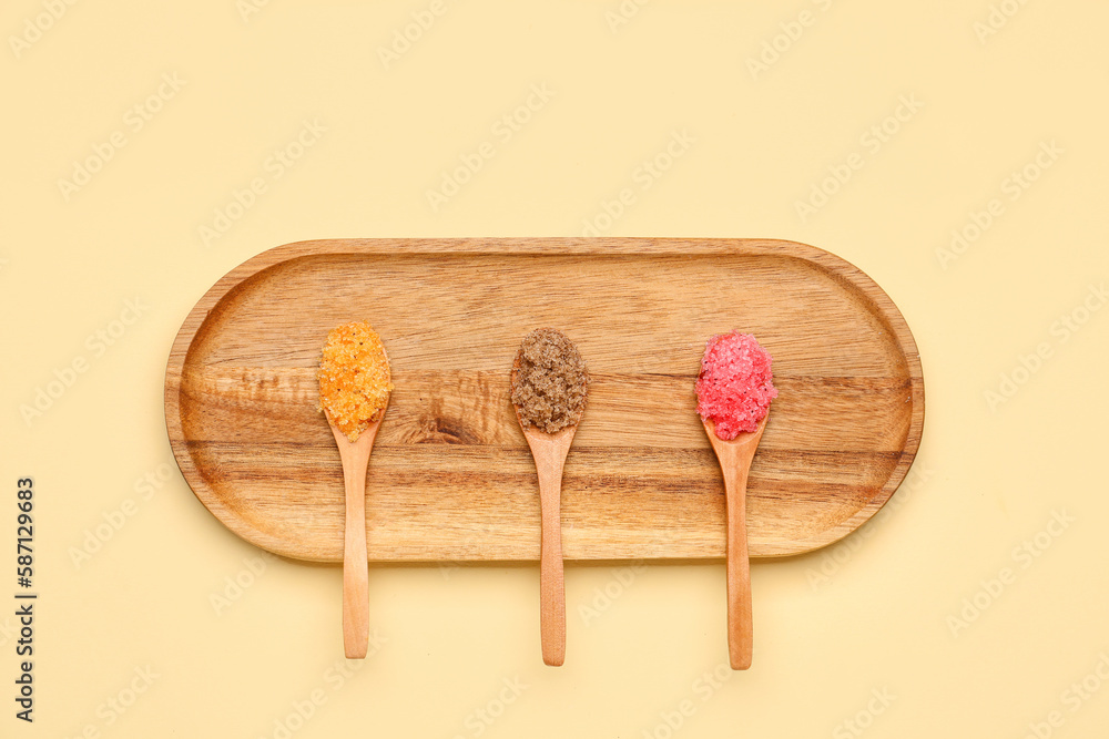 Wooden board with spoons of body scrub on color background