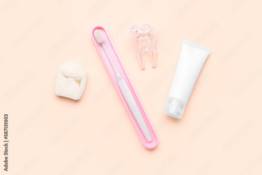 Dental floss, brush, plastic tooth model and tube of paste on beige background