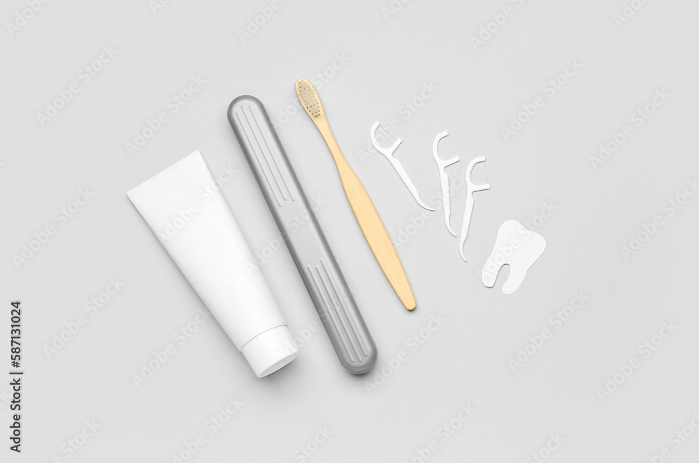 Floss toothpicks, tube of paste, brush and tooth model on grey background