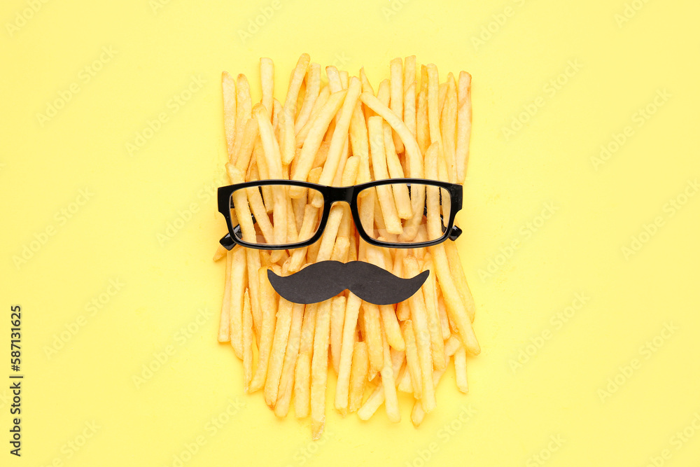 Composition with tasty french fries, glasses and mustache on yellow background