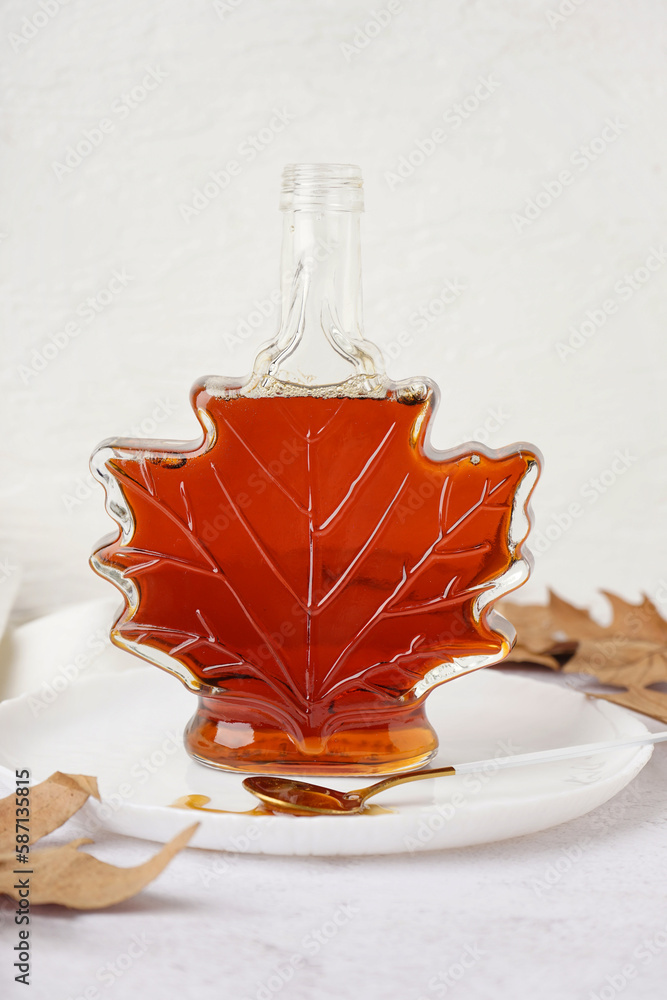 Bottle and spoon of spilled tasty maple syrup on white table