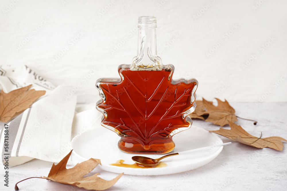 Bottle and spoon of spilled tasty maple syrup on white table