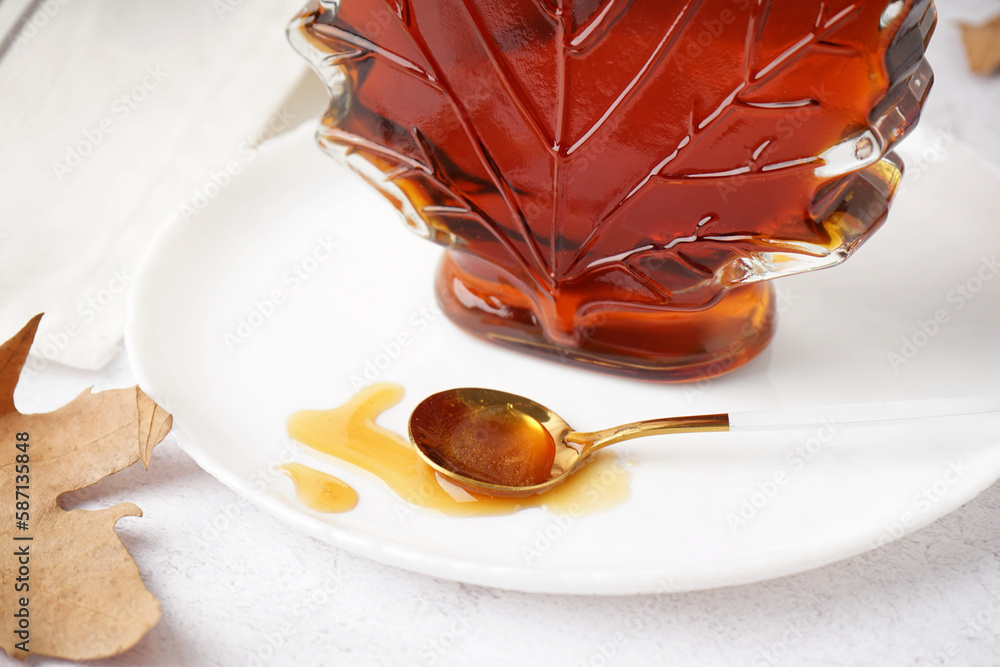 Bottle and spoon of spilled tasty maple syrup on white table