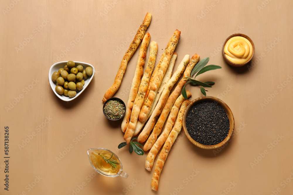 Tasty Italian Grissini with bowls of herbs, sauce and sesame on beige wooden background