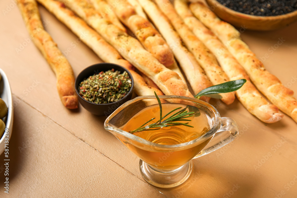 Gravy boat of oil and tasty Italian Grissini on beige wooden background, closeup