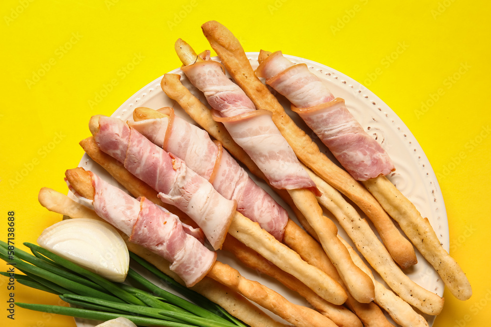 Plate of tasty Italian Grissini with bacon on yellow background, closeup