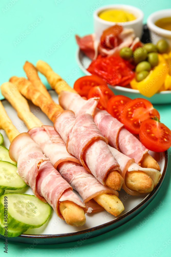 Plate of tasty Italian Grissini with bacon on turquoise background, closeup