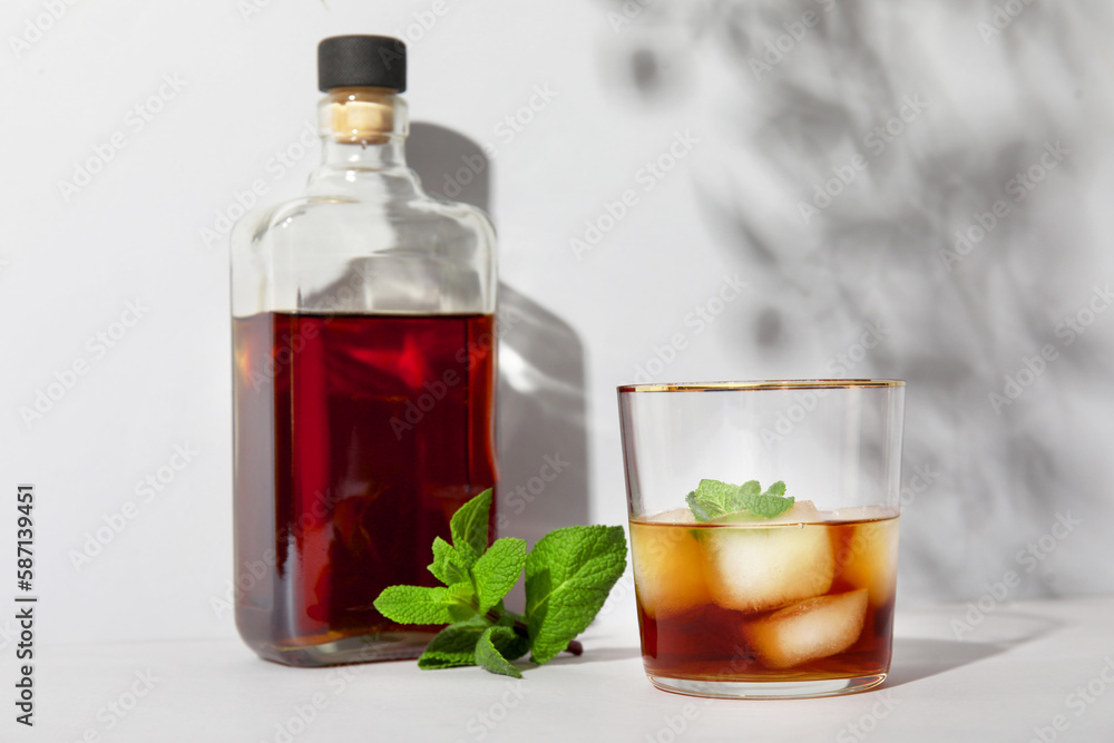 Bottle and glass of cold rum on grey background