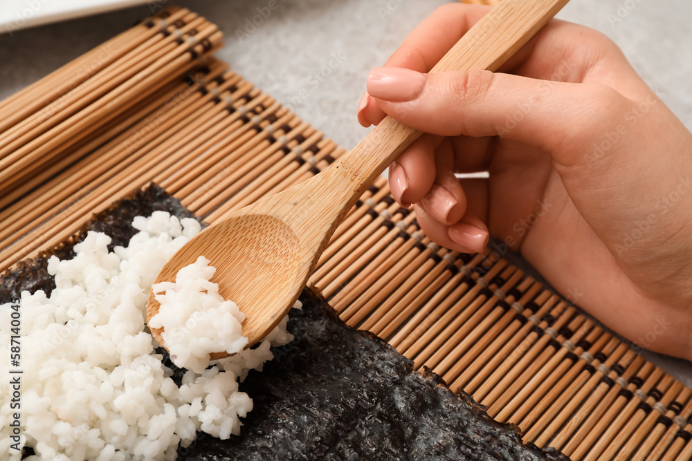 Woman preparing sushi rolls on light background, closeup